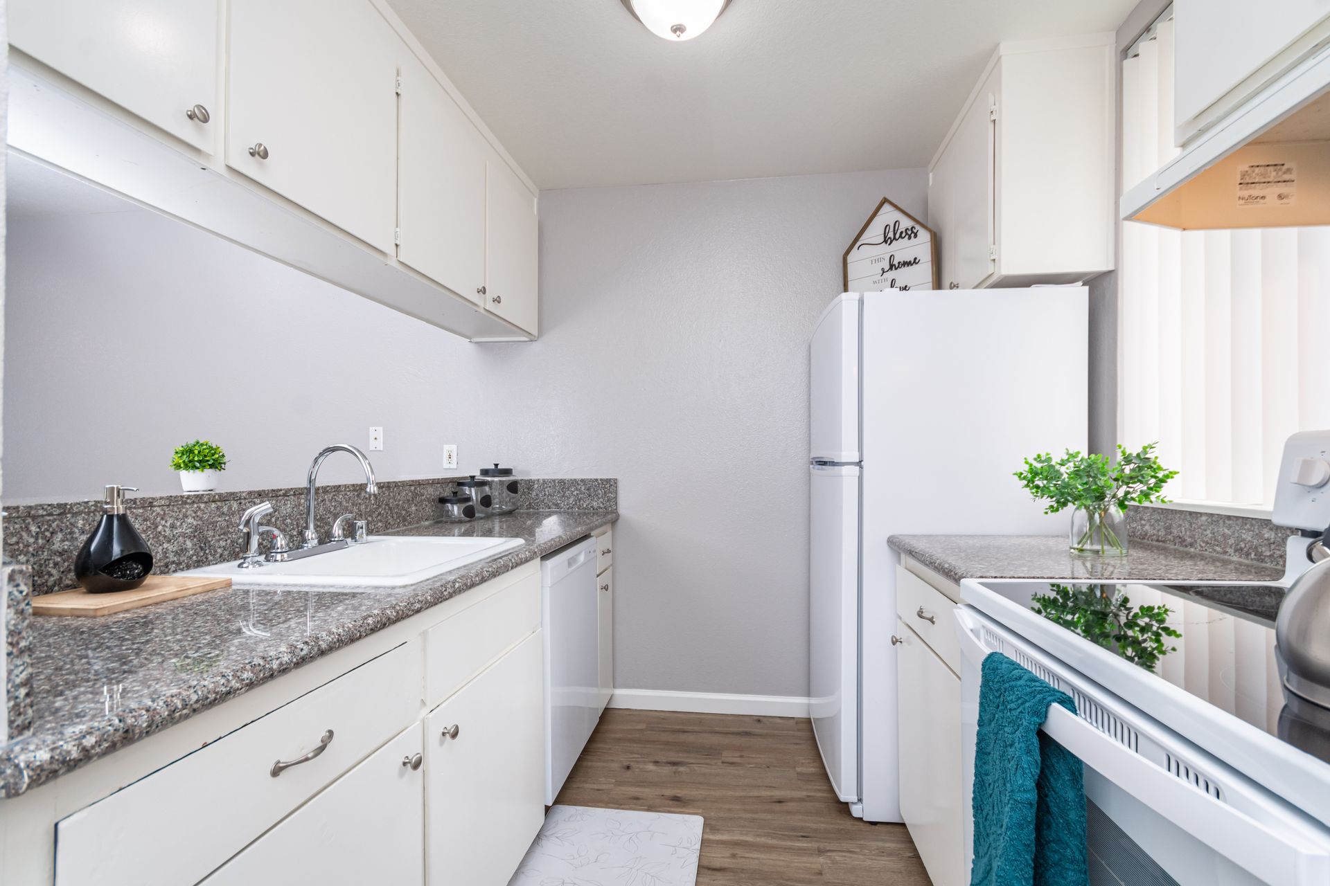 Bright white kitchen with granite counters, white cabinets, stove, and refrigerator