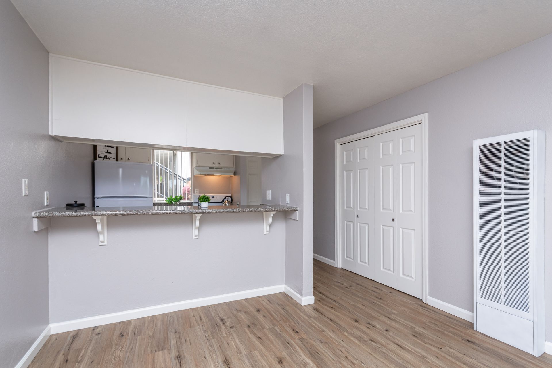 Empty apartment living area with breakfast bar, white closet doors, and wood flooring