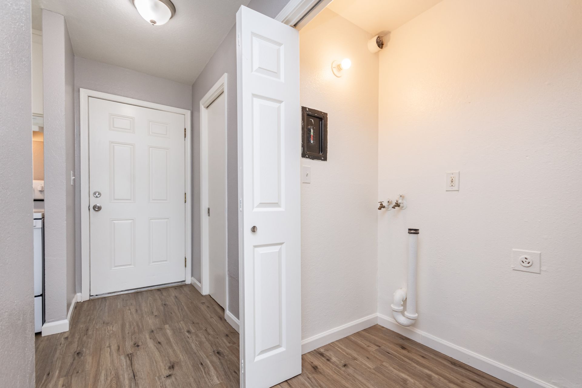 Small white hallway with wood floors, a front door, closet doors, and a laundry hookup.