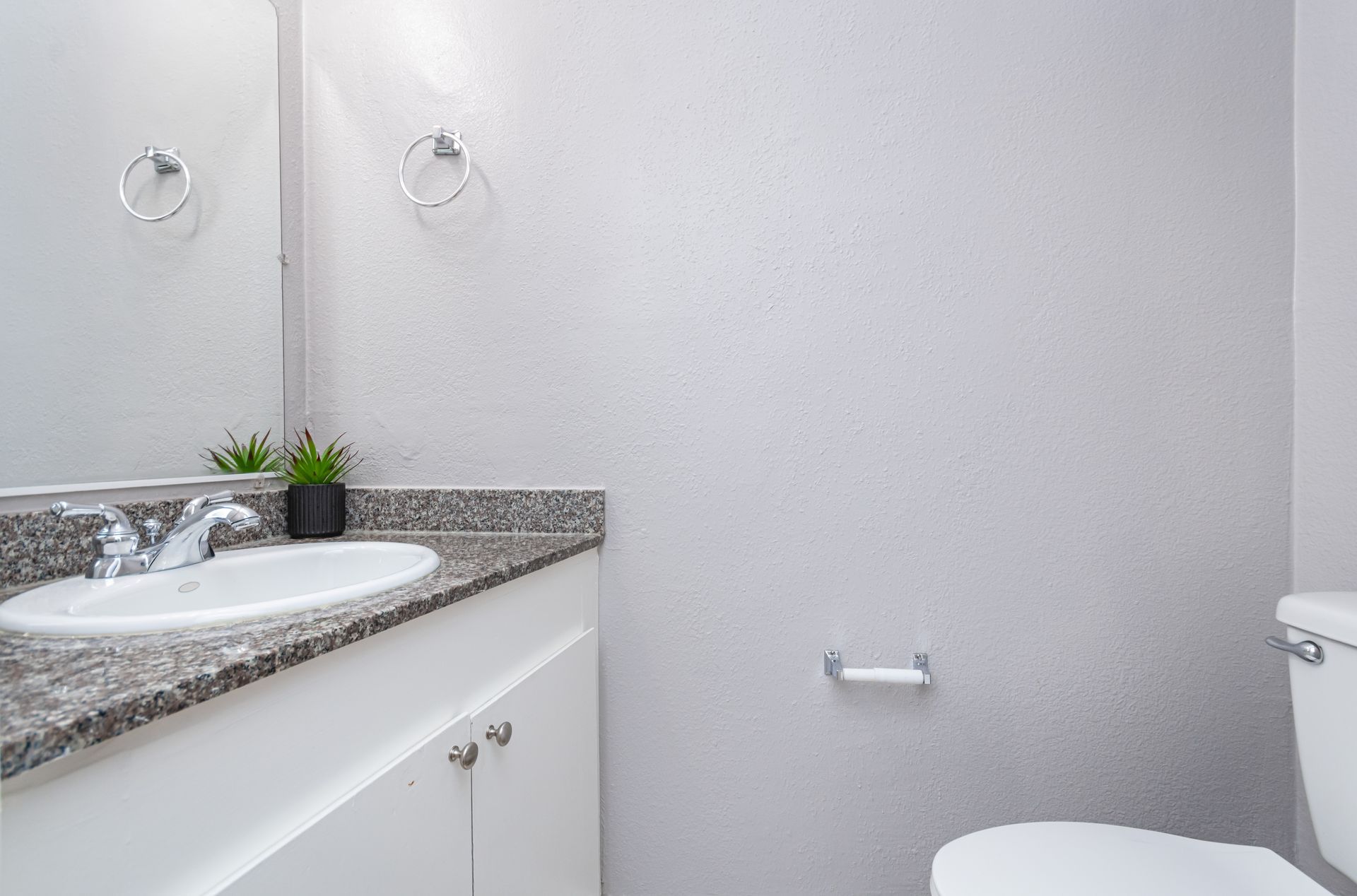 Modern bathroom with a white sink, granite countertop, wall mirror, and toilet.