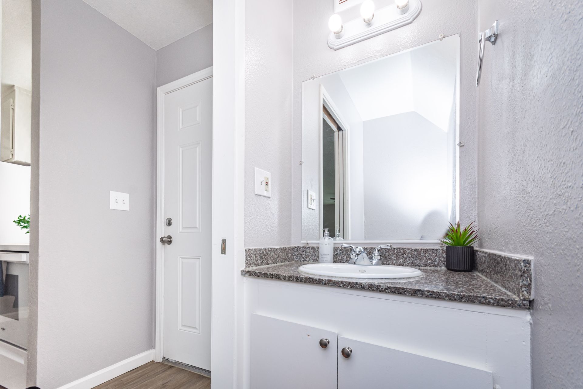 Bright bathroom vanity with mirror, granite countertop, and white cabinets in a light gray hallway