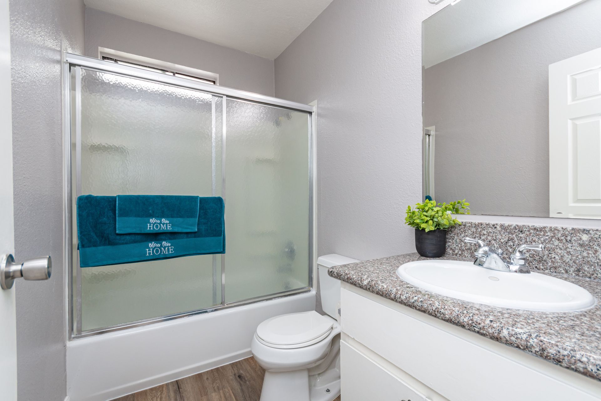 Small bathroom with frosted shower doors, toilet, white sink vanity, and a gray countertop.