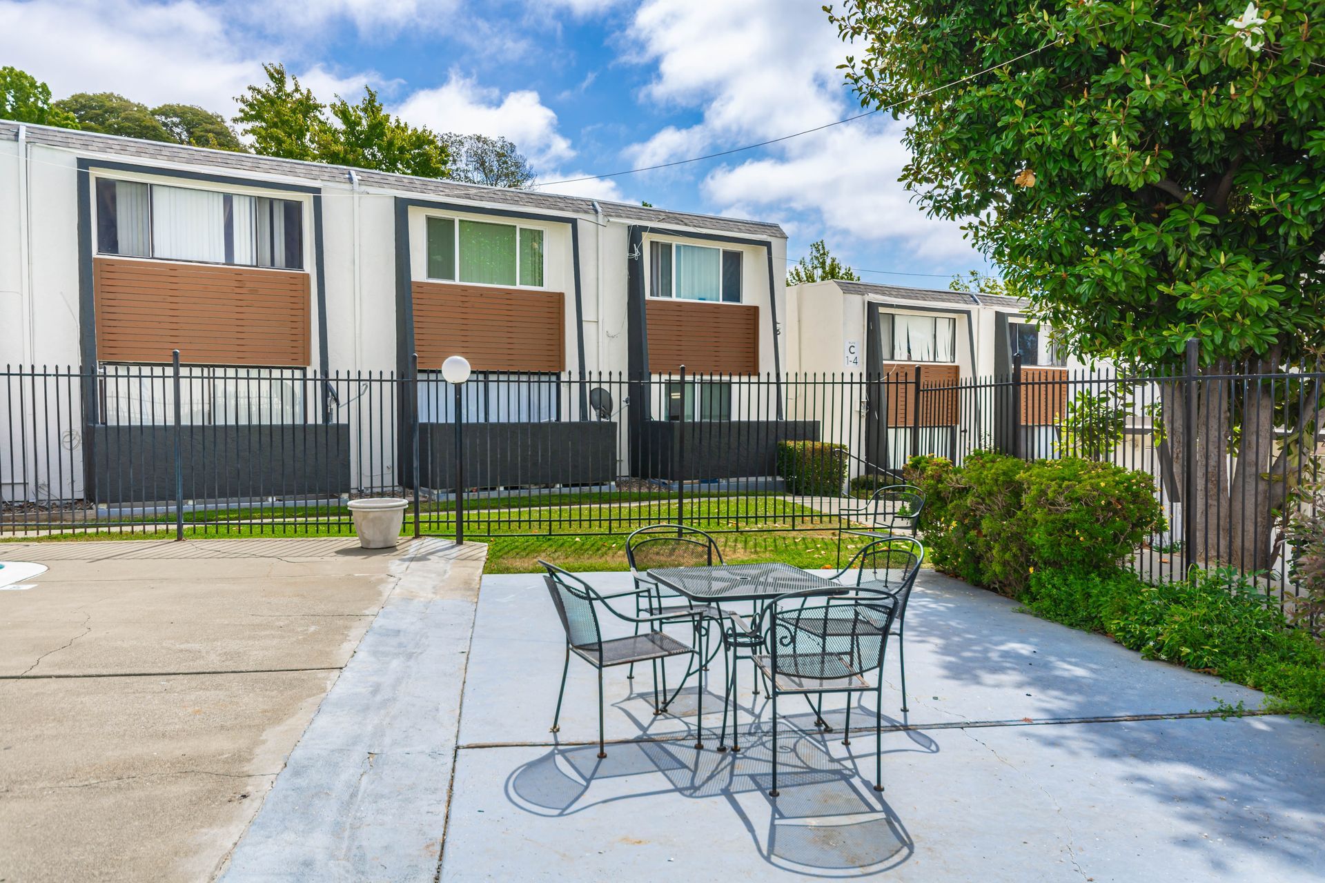 Patio with metal table and chairs beside a townhouse row and black fence under a blue sky