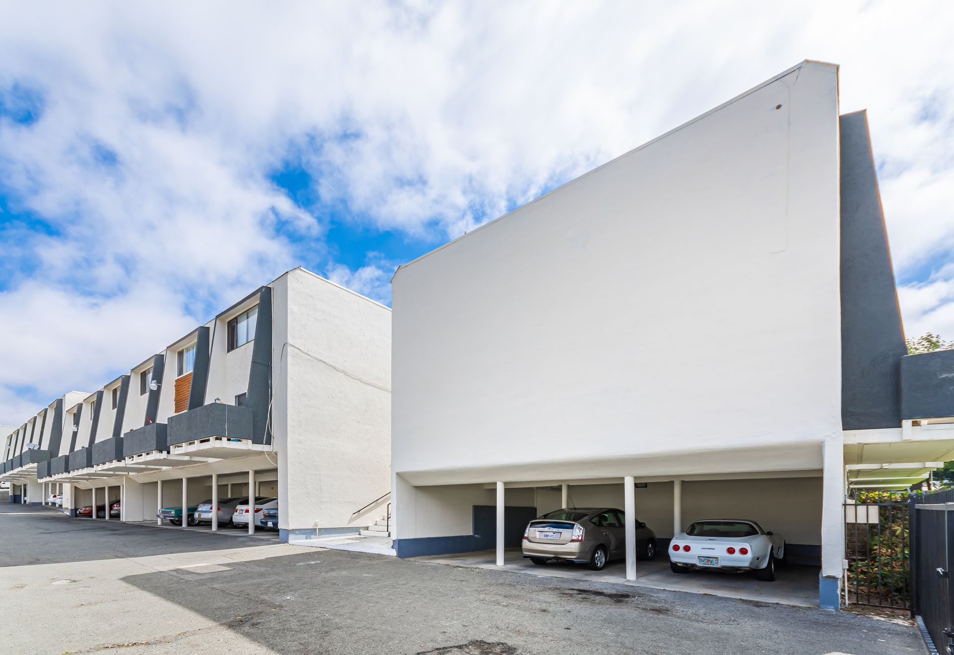 Modern row of white townhouses with covered parking and two cars under a bright cloudy sky