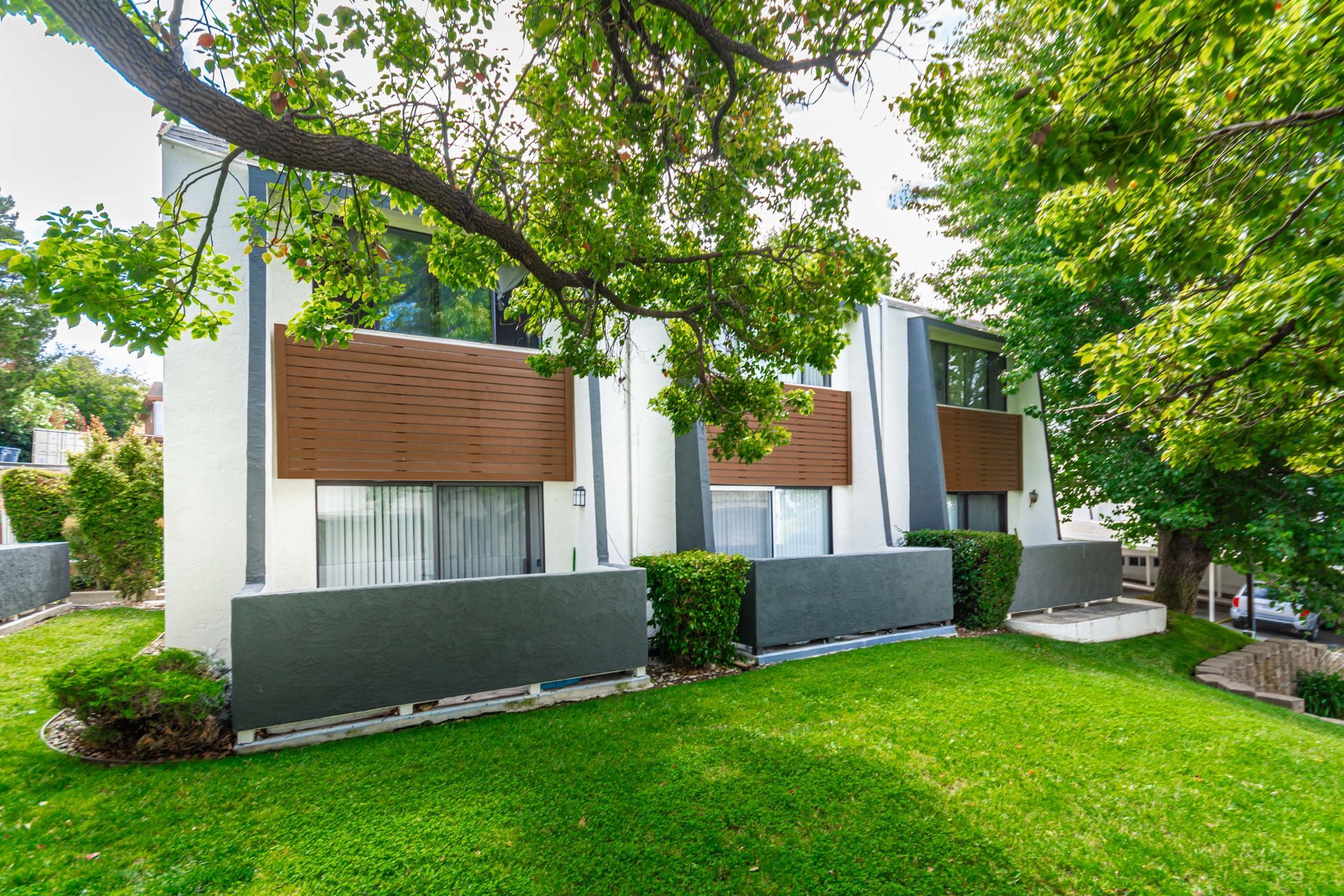 Modern white house with brown shutters, large windows, and a green lawn under leafy trees