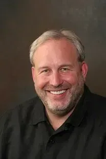 A man with a beard is smiling for the camera while wearing a black shirt.