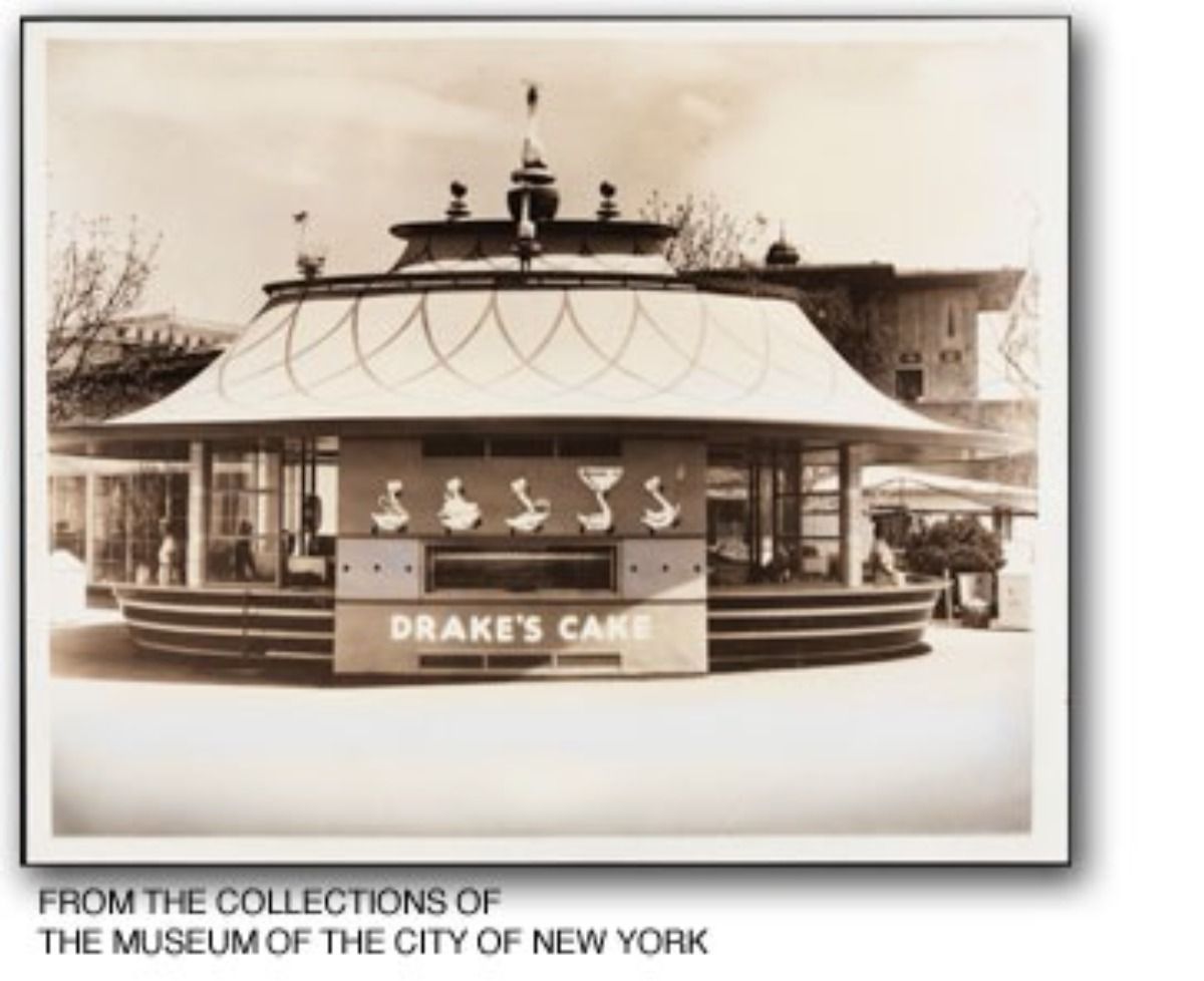 A vintage, sepia-toned photo of a circular Drake's Cake stand with a wide, tiered roof, located at a fair or park.