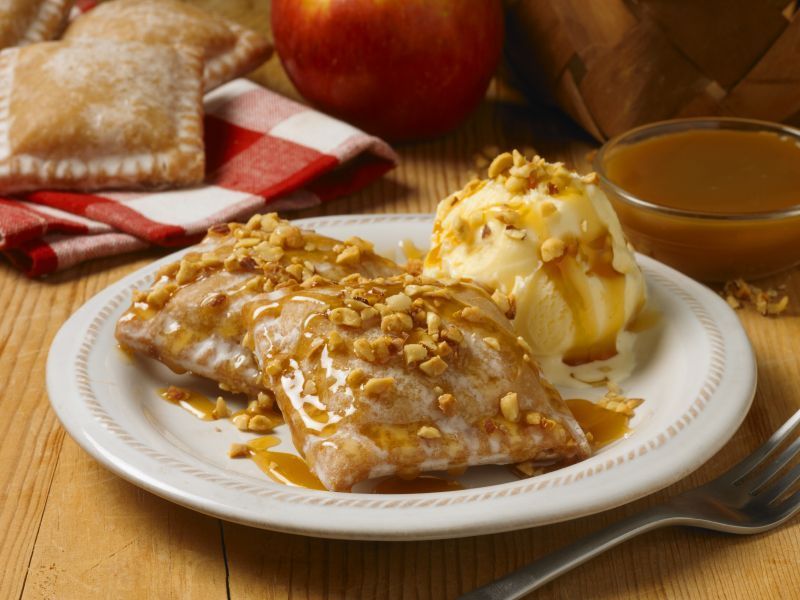 Fried apple pastries topped with nuts and caramel sauce, served on a plate with a scoop of vanilla ice cream.