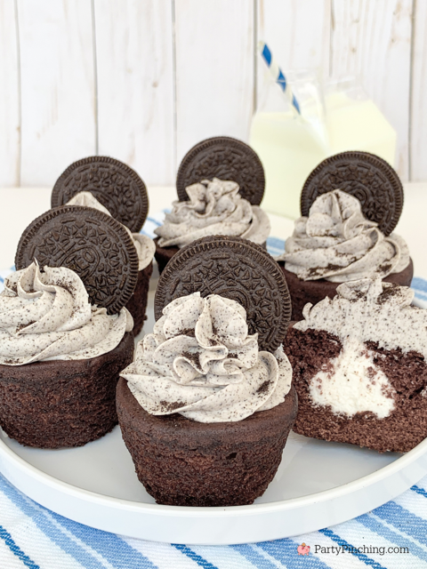 Chocolate cupcakes topped with cookies and cream frosting and sandwich cookies, arranged on a plate with a glass of milk.