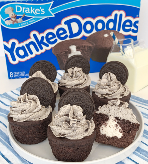 A box of Drake’s Yankee Doodles sits behind a plate of chocolate cupcakes topped with cookies and cream frosting.