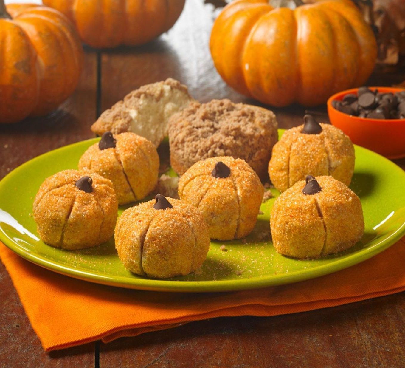 Pumpkin-shaped treats coated in cinnamon sugar and topped with chocolate chips, served on a green plate with pumpkins.