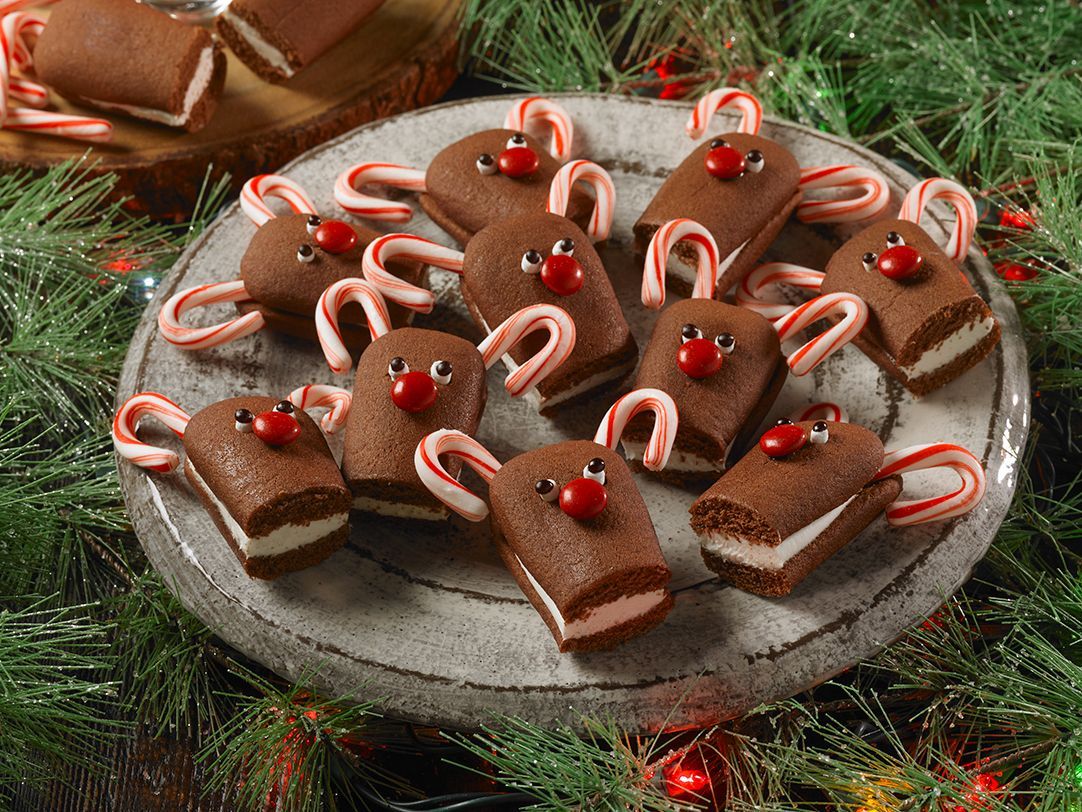 Small chocolate cream-filled cakes decorated as reindeer with candy cane antlers and red candy noses on a grey plate.