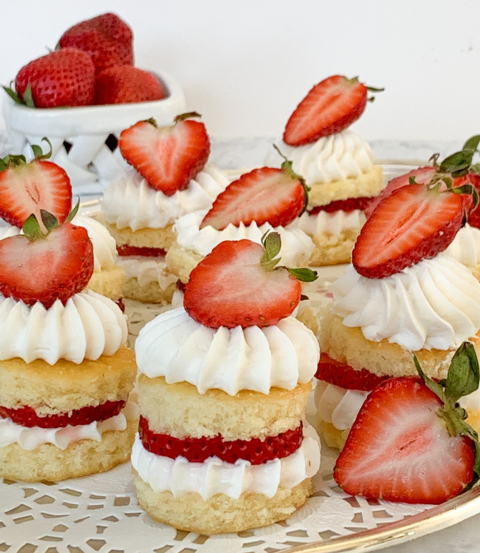 Mini strawberry shortcake desserts topped with whipped cream and sliced strawberries, arranged on a decorative plate.