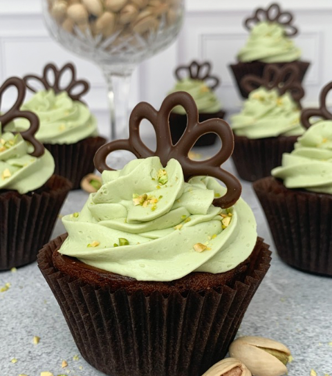 Close-up of pistachio-frosted cupcakes made with Drake's Cakes Yankee Doodles, sitting on a gray surface with a bright blue background.