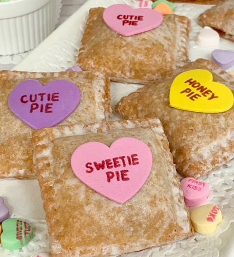 Heart-shaped conversation candies topping square, glazed hand pies on a white lace-trimmed plate.