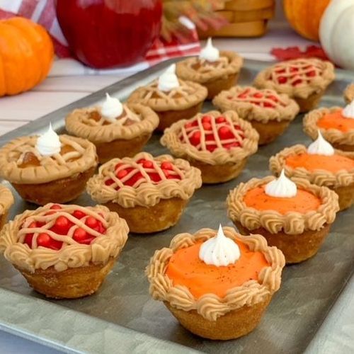 A metal tray filled with mini pies, including lattice-topped fruit pies and orange pumpkin pies with piped crusts and cream.