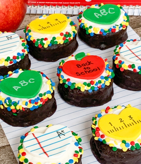 Back-to-school themed mini cakes decorated with heart-shaped toppers, including rulers, notebooks, and apples.