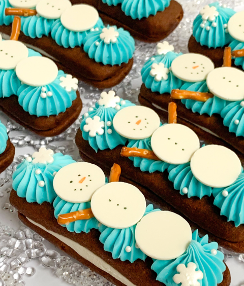 Chocolate cookies decorated with blue frosting swirls, white chocolate snowman faces, and pretzel stick arms.