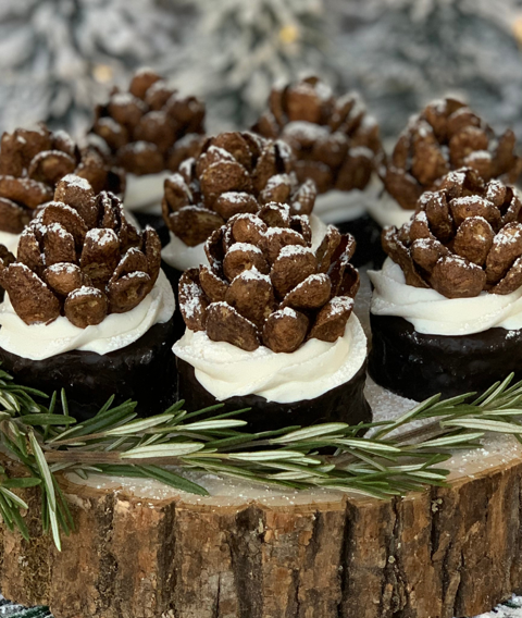 Chocolate pinecone treats made with cereal, sitting on white frosting and dark bases, decorated with edible snow.