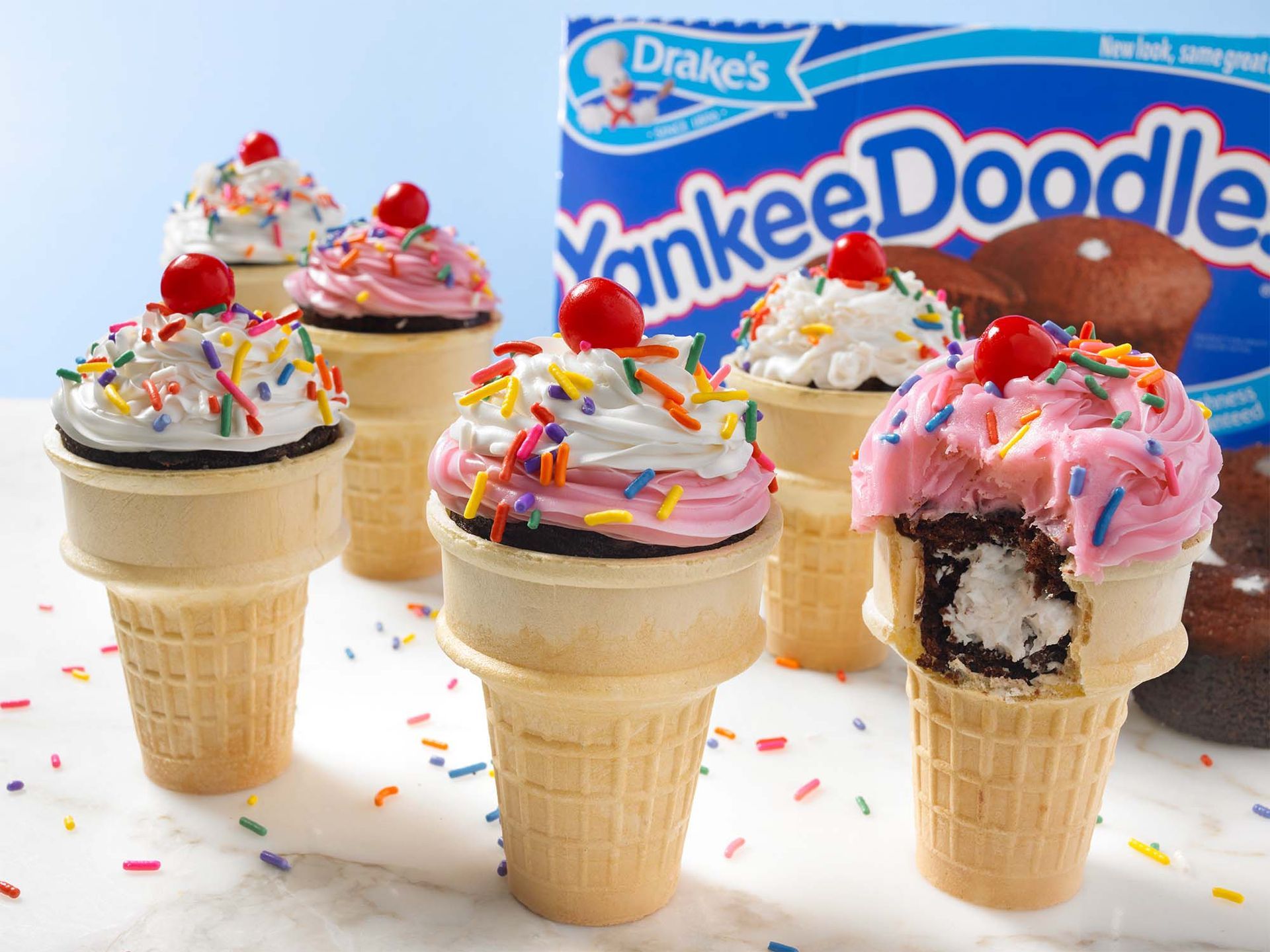 three cupcakes decorated to look like birthday cakes with a yankee doodle carton in the background