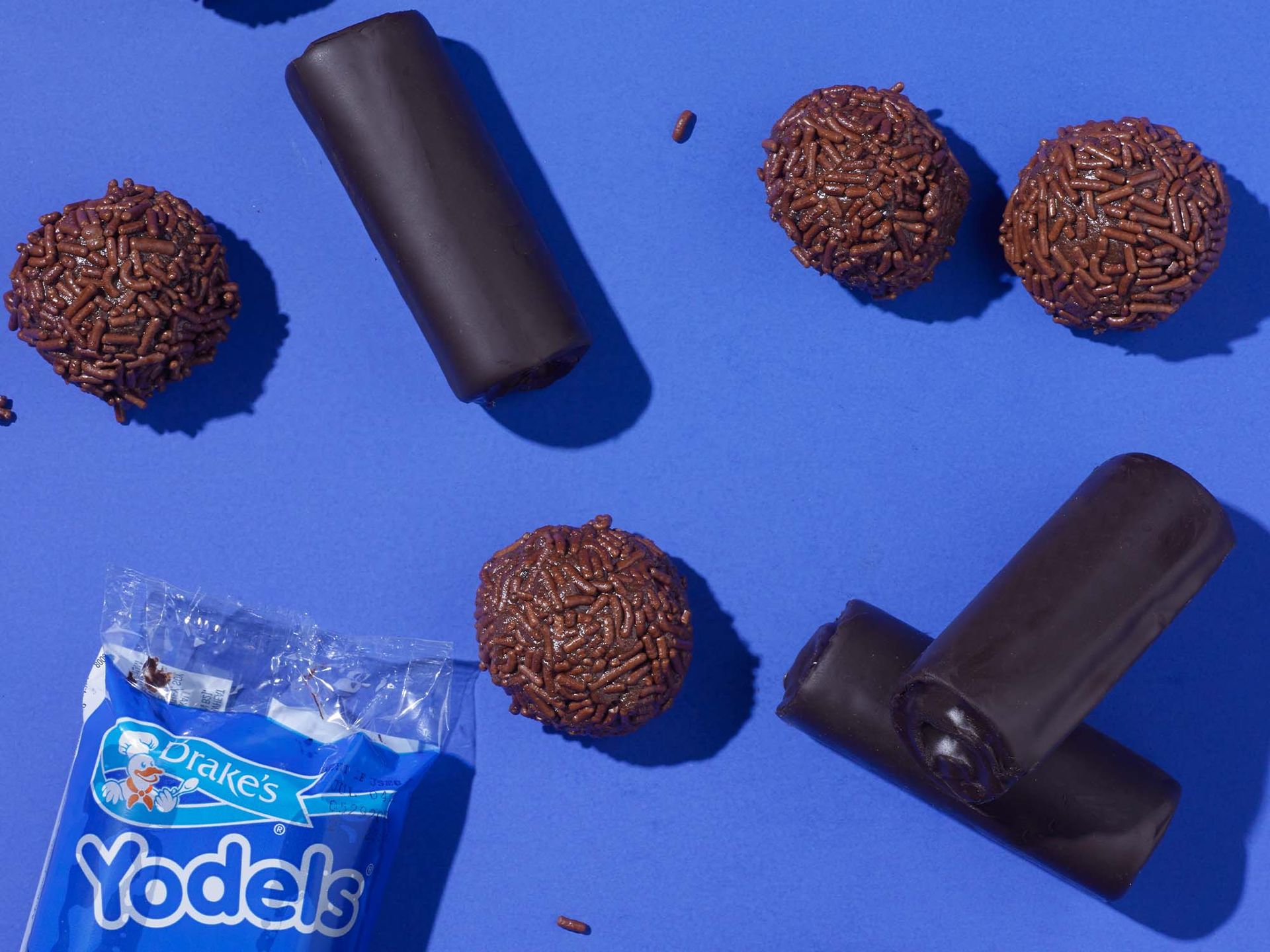 Drake’s Yodels snack cakes and chocolate-covered round treats arranged on a vibrant blue background.