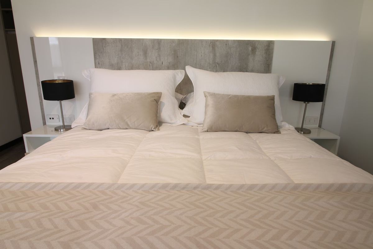Una cama cuidadosamente hecha con almohadas beige, sábanas blancas y lámparas negras en las mesitas de noche de un dormitorio moderno.