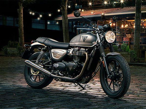 A triumph motorcycle is parked on a cobblestone street at night.