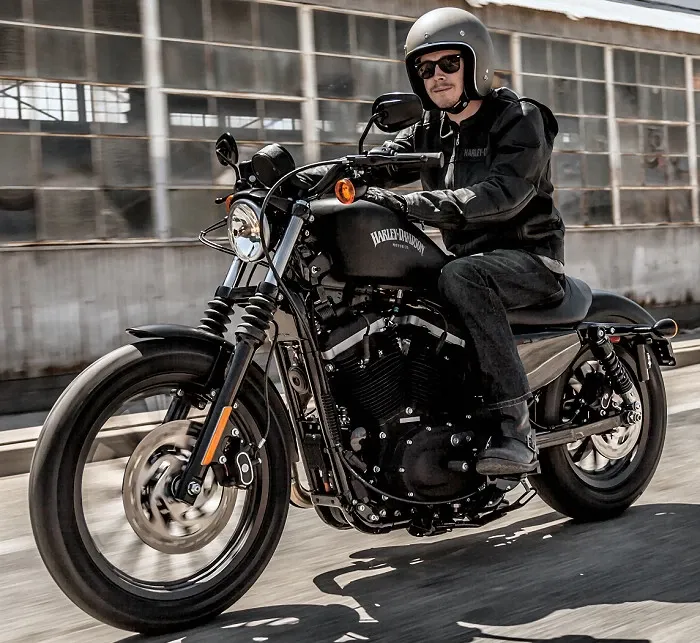 A man is riding a black harley davidson motorcycle on a city street.