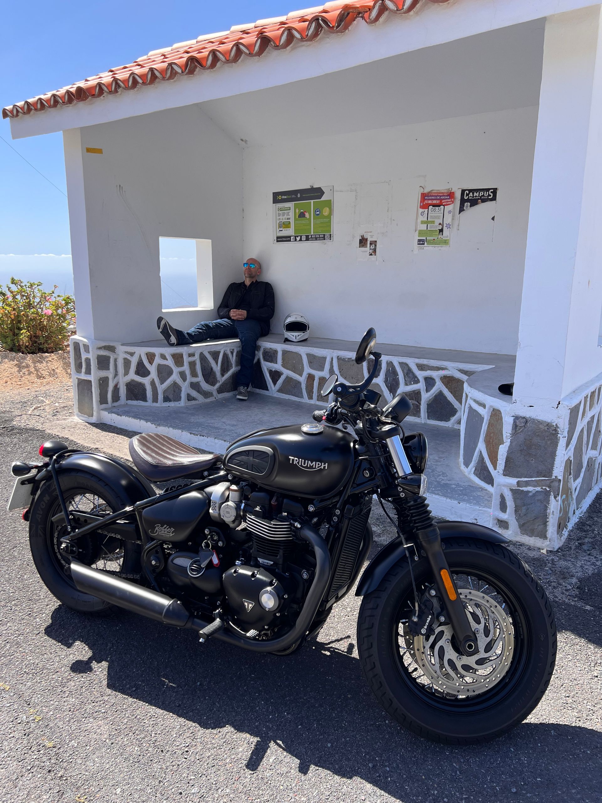 A man is sitting on a porch next to a motorcycle.