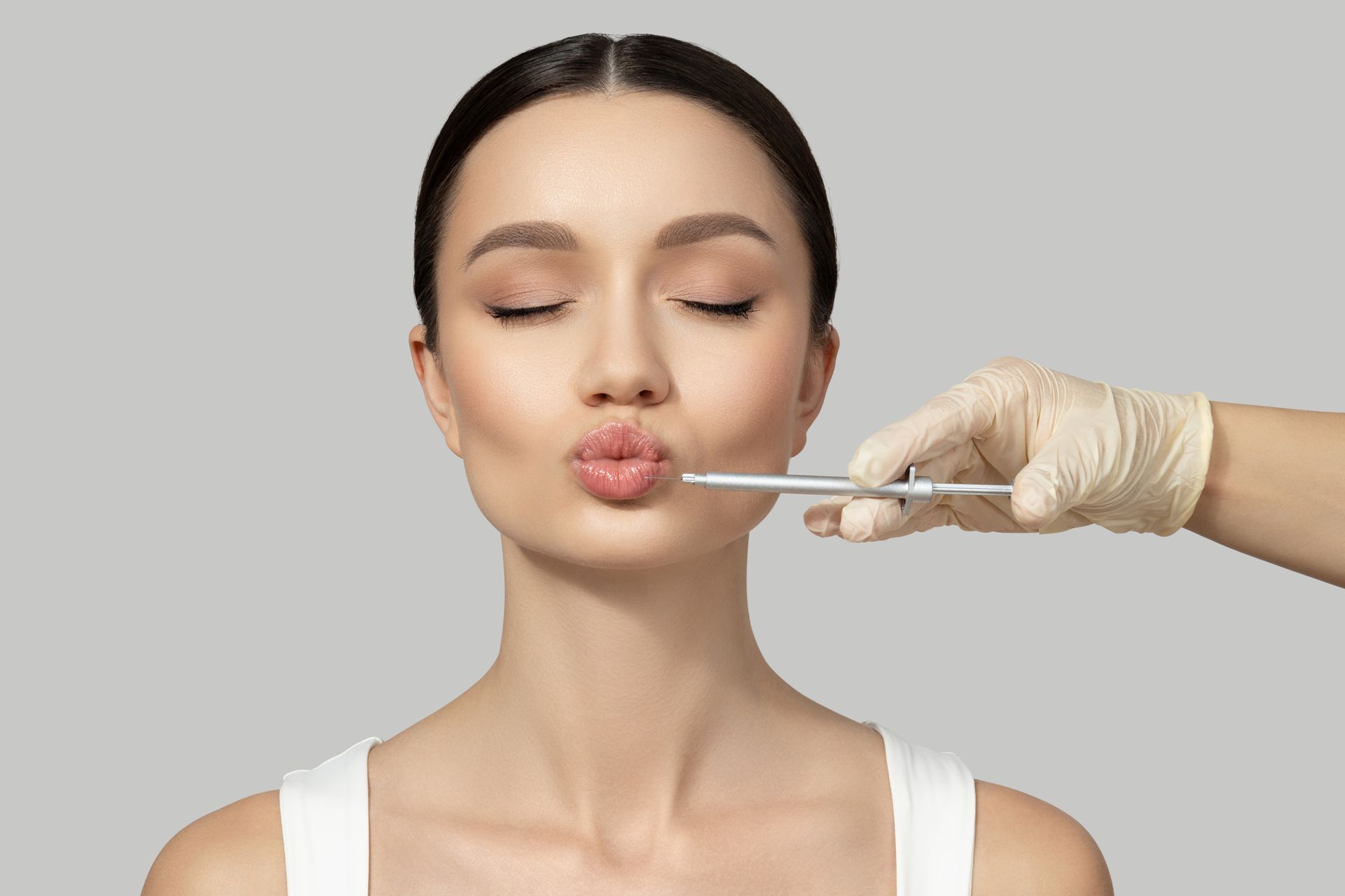 Woman receiving a cosmetic lip treatment with a gloved hand using a syringe-like tool