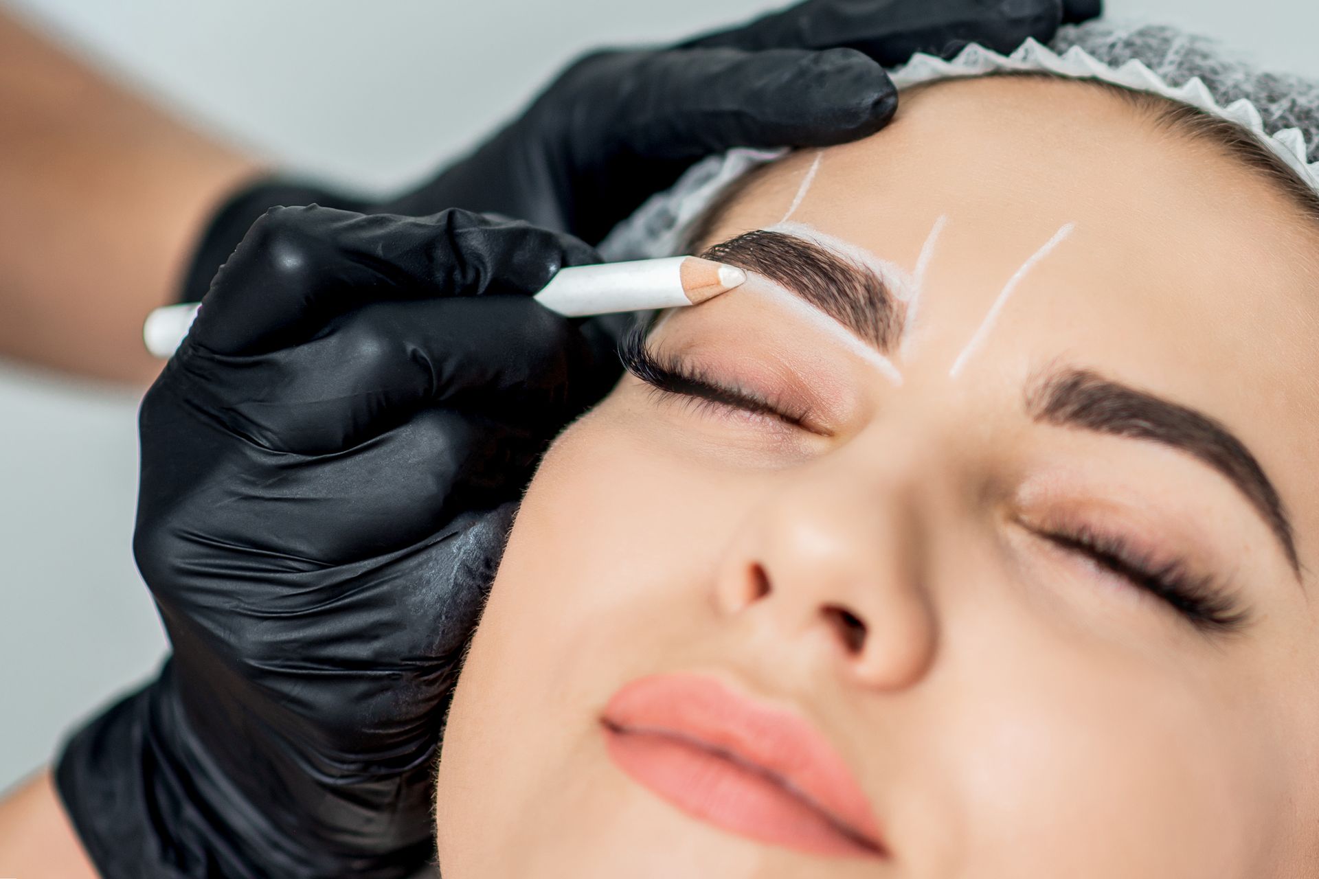 Gloved hand applying eyebrow makeup to a closed-eyed person’s brow
