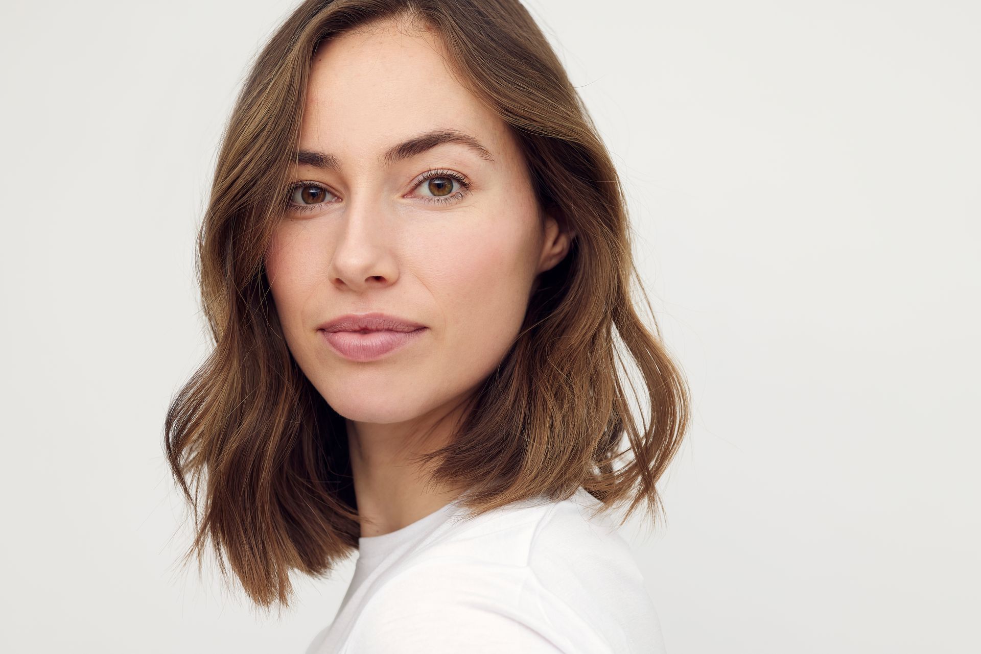 A woman with brown hair is wearing a white shirt and looking at the camera.