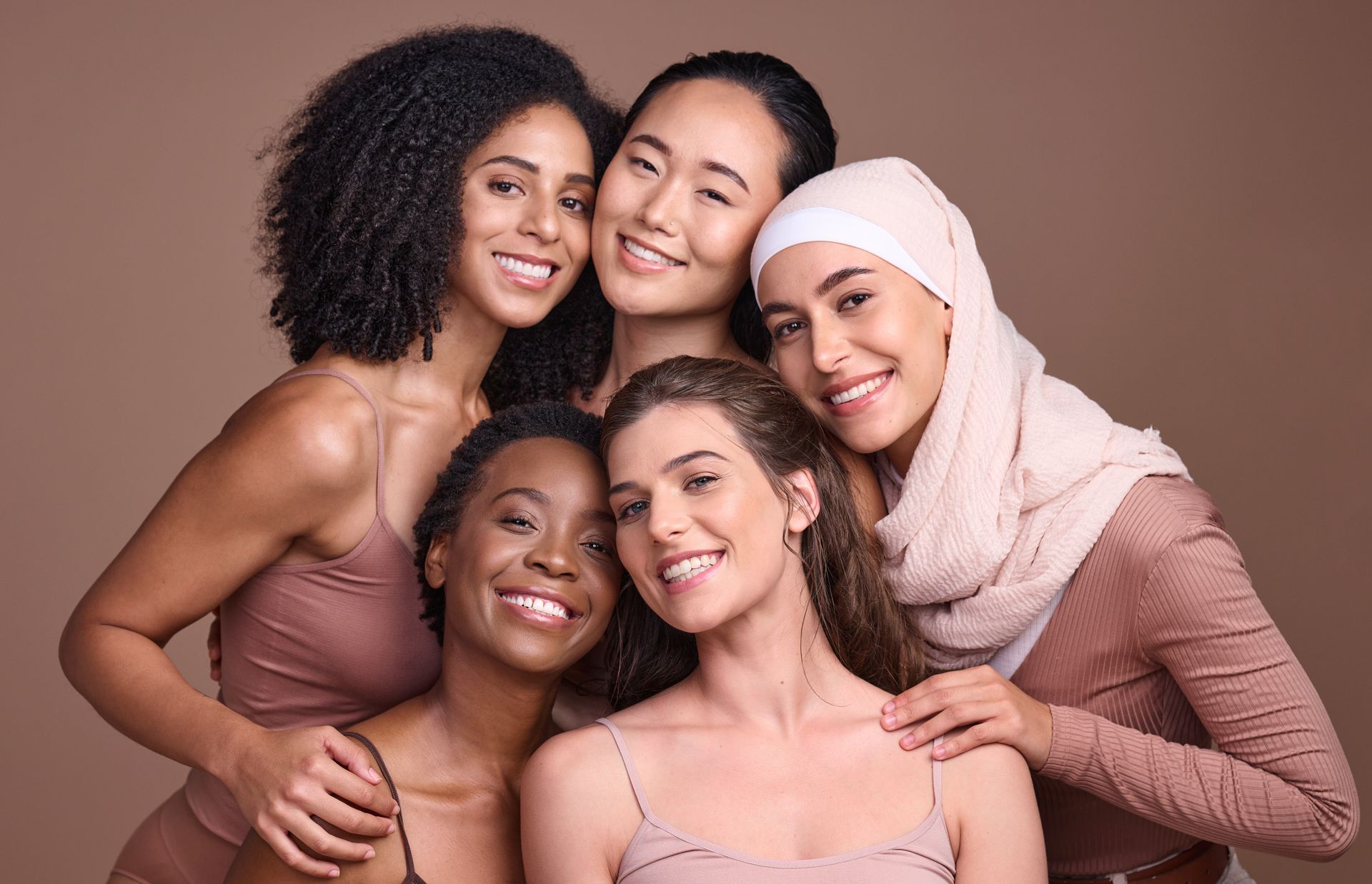 Five smiling friends posing closely together against a soft pink studio backdrop.