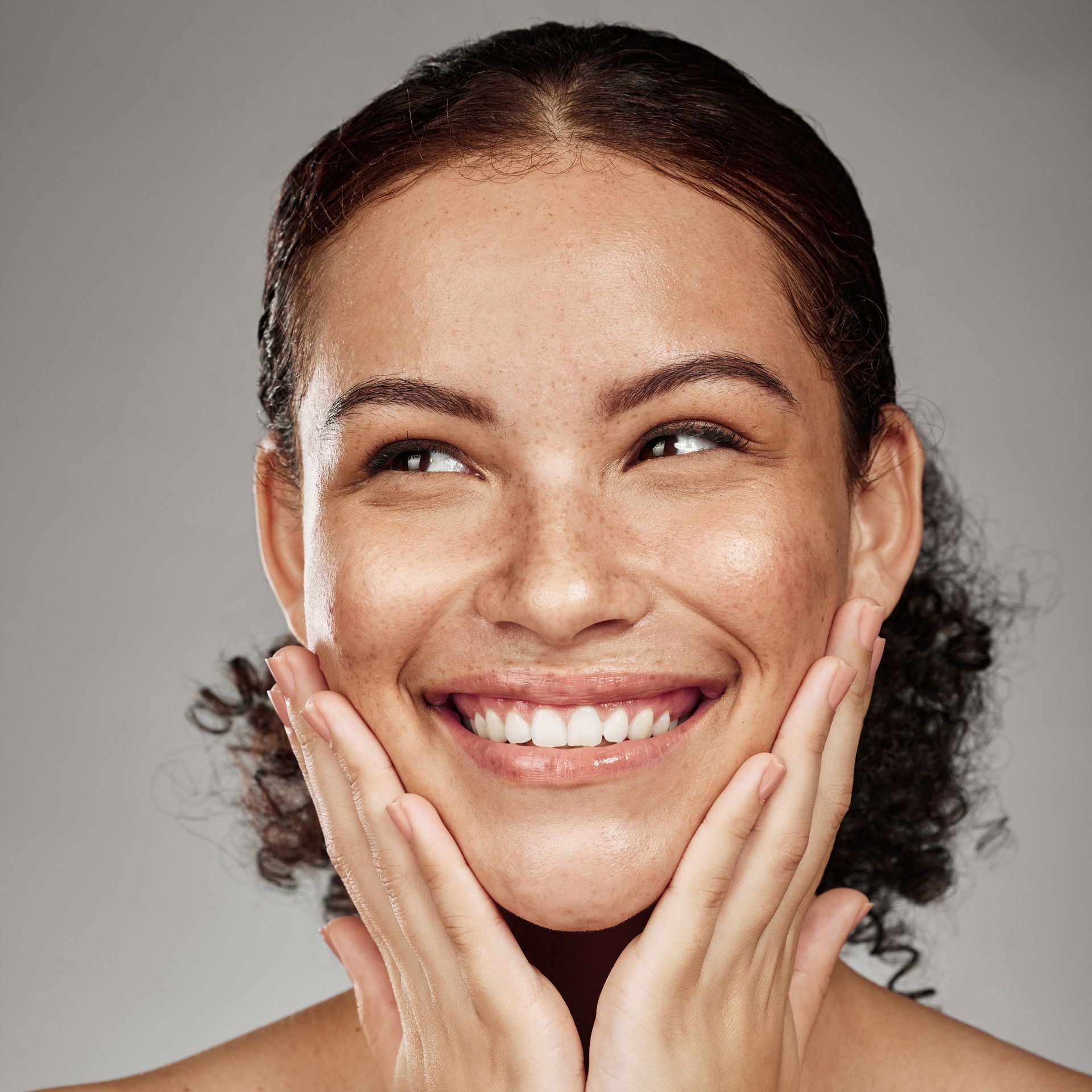 A woman is smiling and touching her face with her hands.