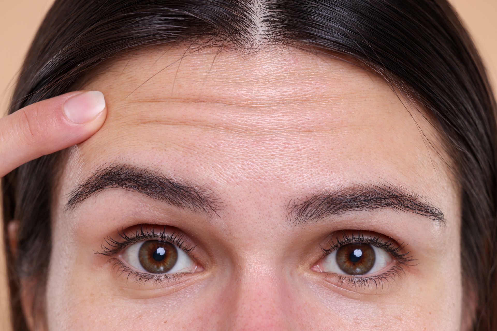 Close-up of a person’s forehead and eyes with a finger pointing to a wrinkle line