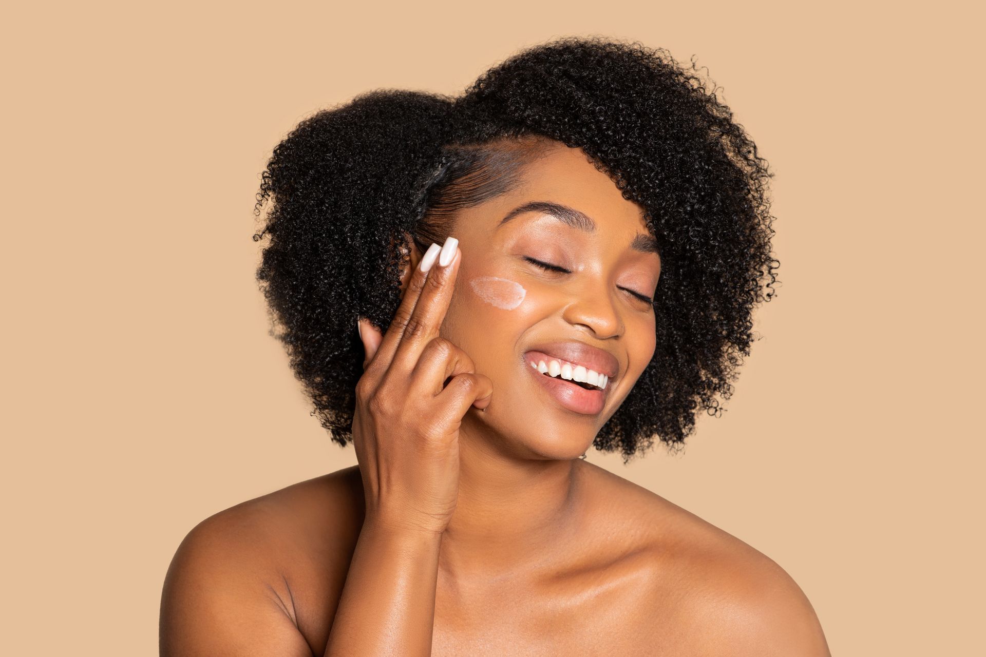A woman is smiling while applying cream to her face.