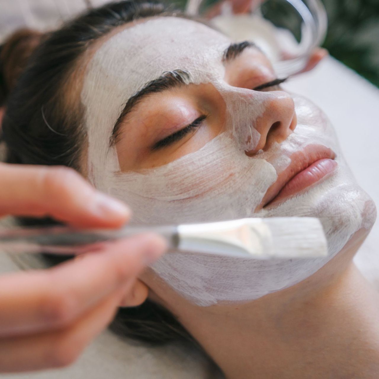 A woman is getting a white mask on her face