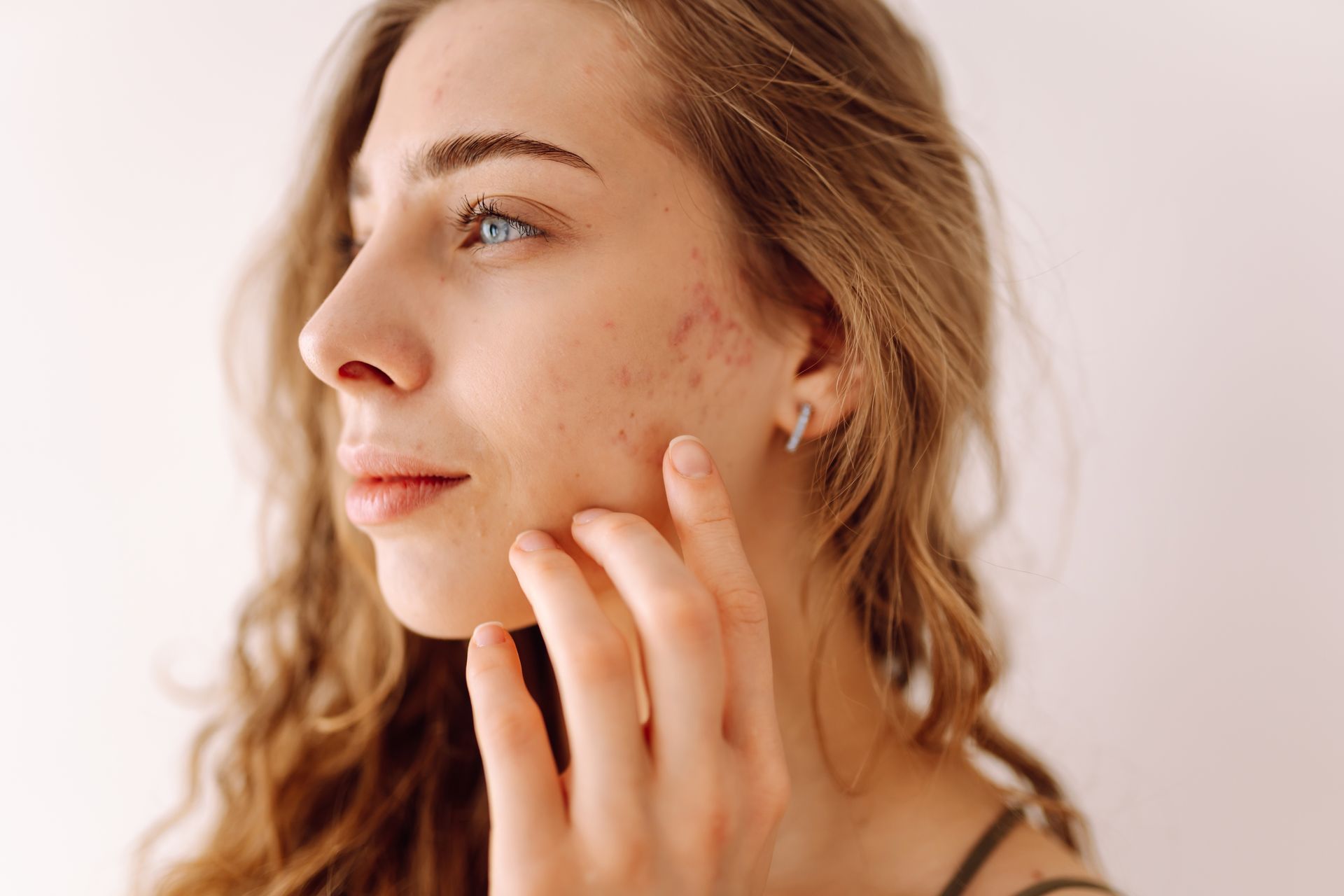 Close-up of a person in profile touching their cheek against a soft white background
