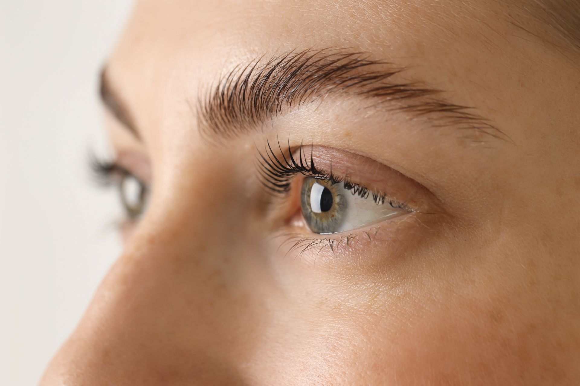 Close-up of a person’s eye and eyebrow in soft light, looking to the right