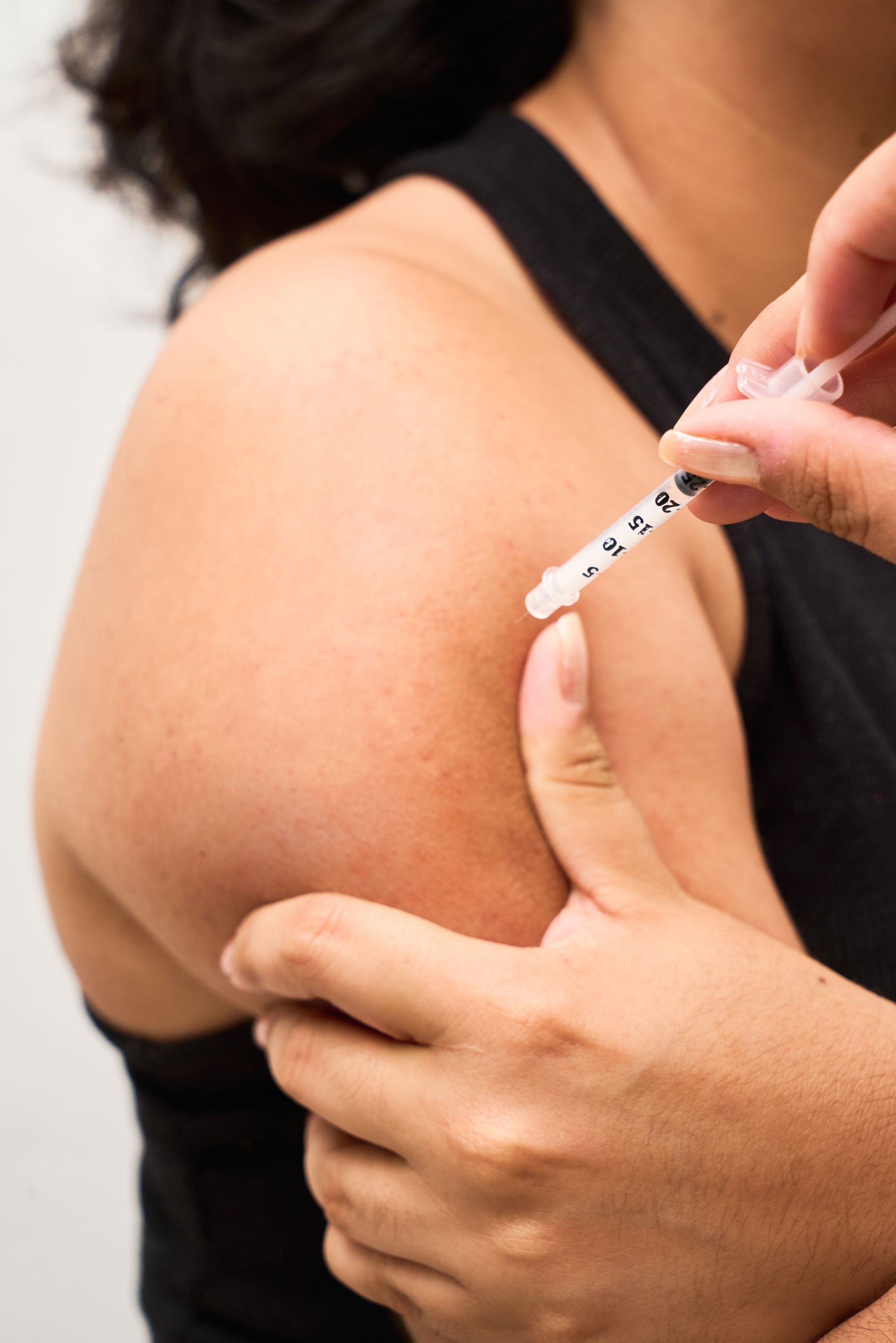 Arm receiving a vaccine injection with a syringe held by another person