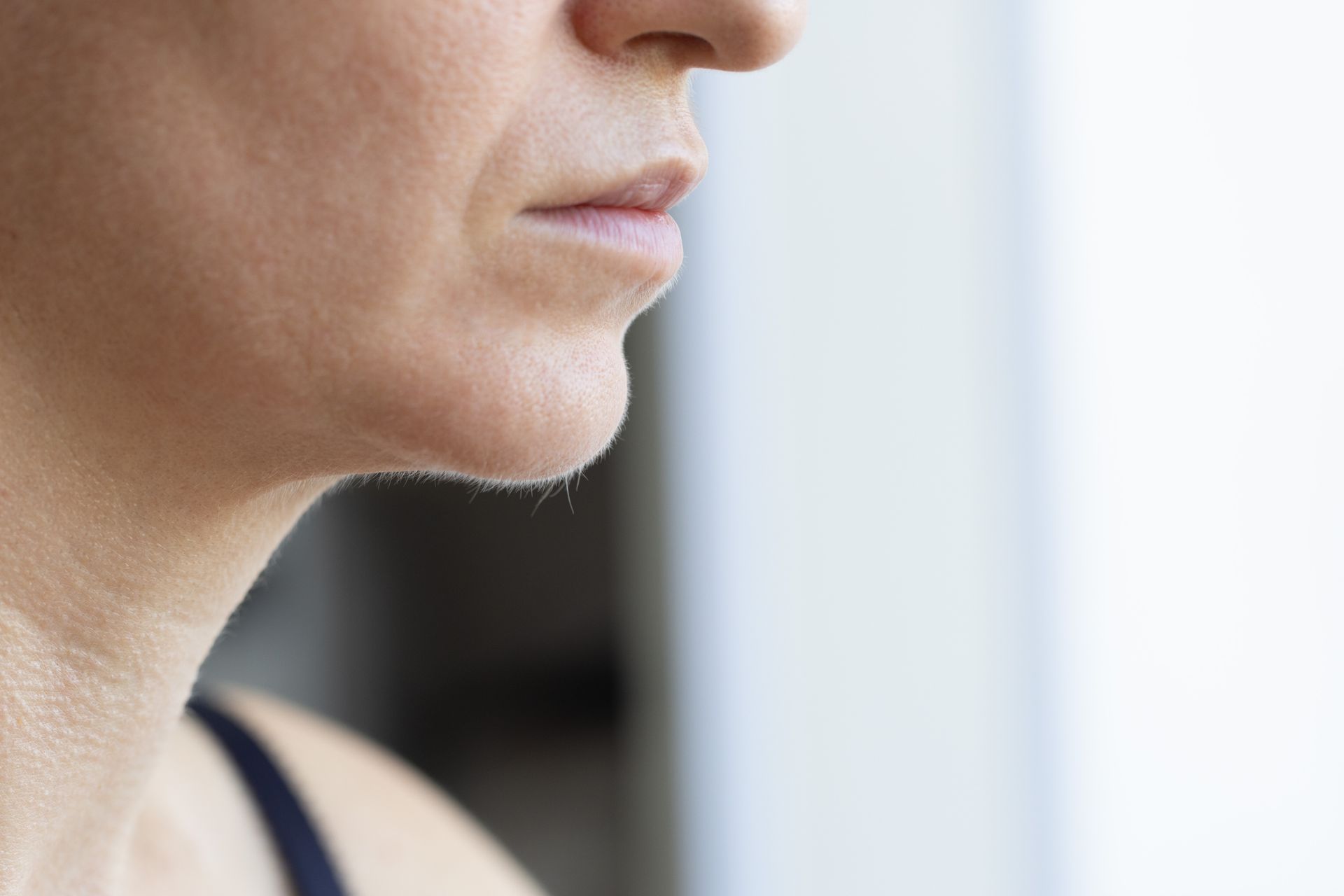 Close-up side profile of a person’s lower face and neck against a softly blurred background