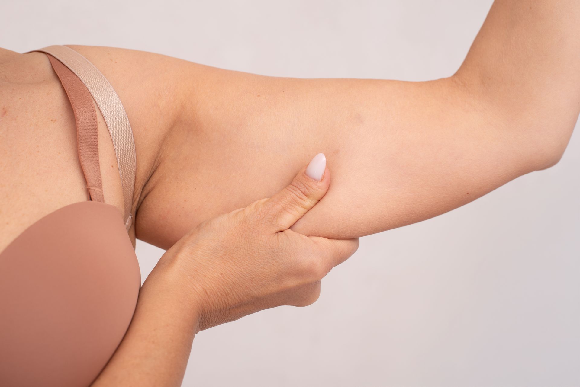 Close-up of a person pinching upper arm skin, showing arm fat and body texture