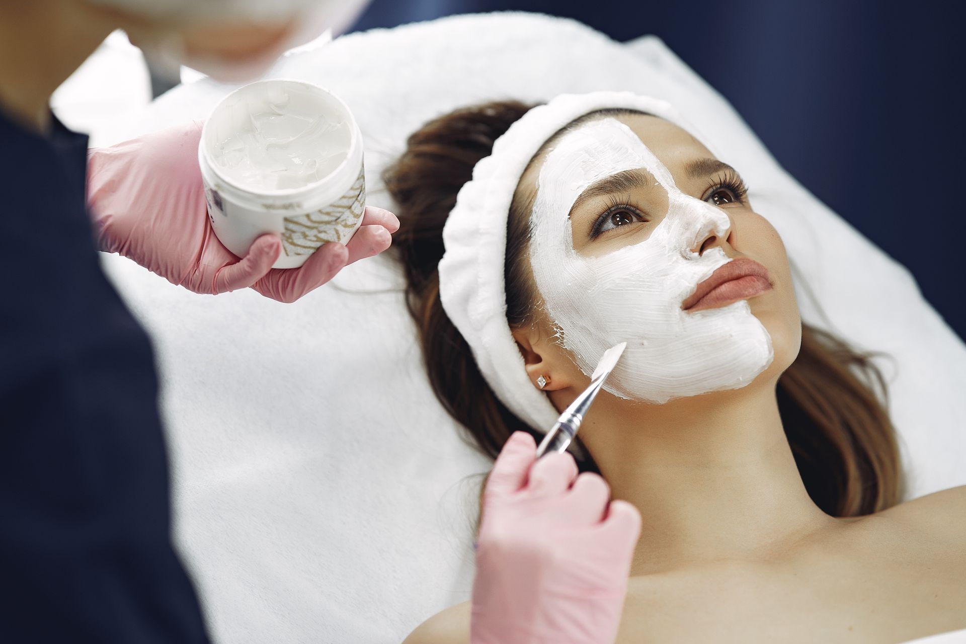 Facial spa treatment with white mask being applied to a reclining client