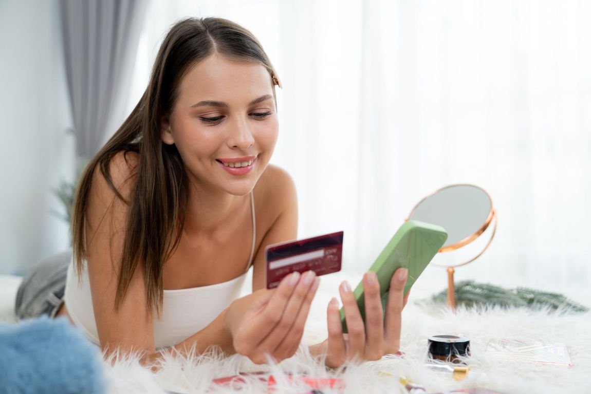 A woman is laying on the floor holding a credit card and a cell phone.