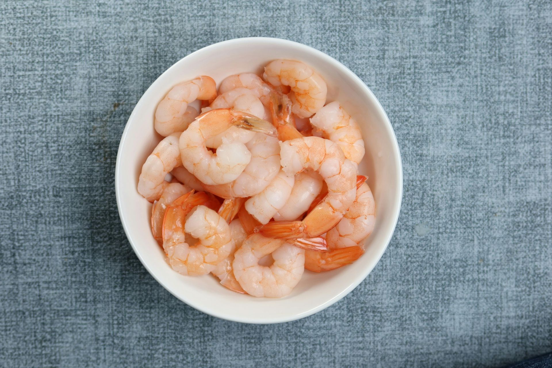 Bowl of cooked shrimp on a blue fabric surface
