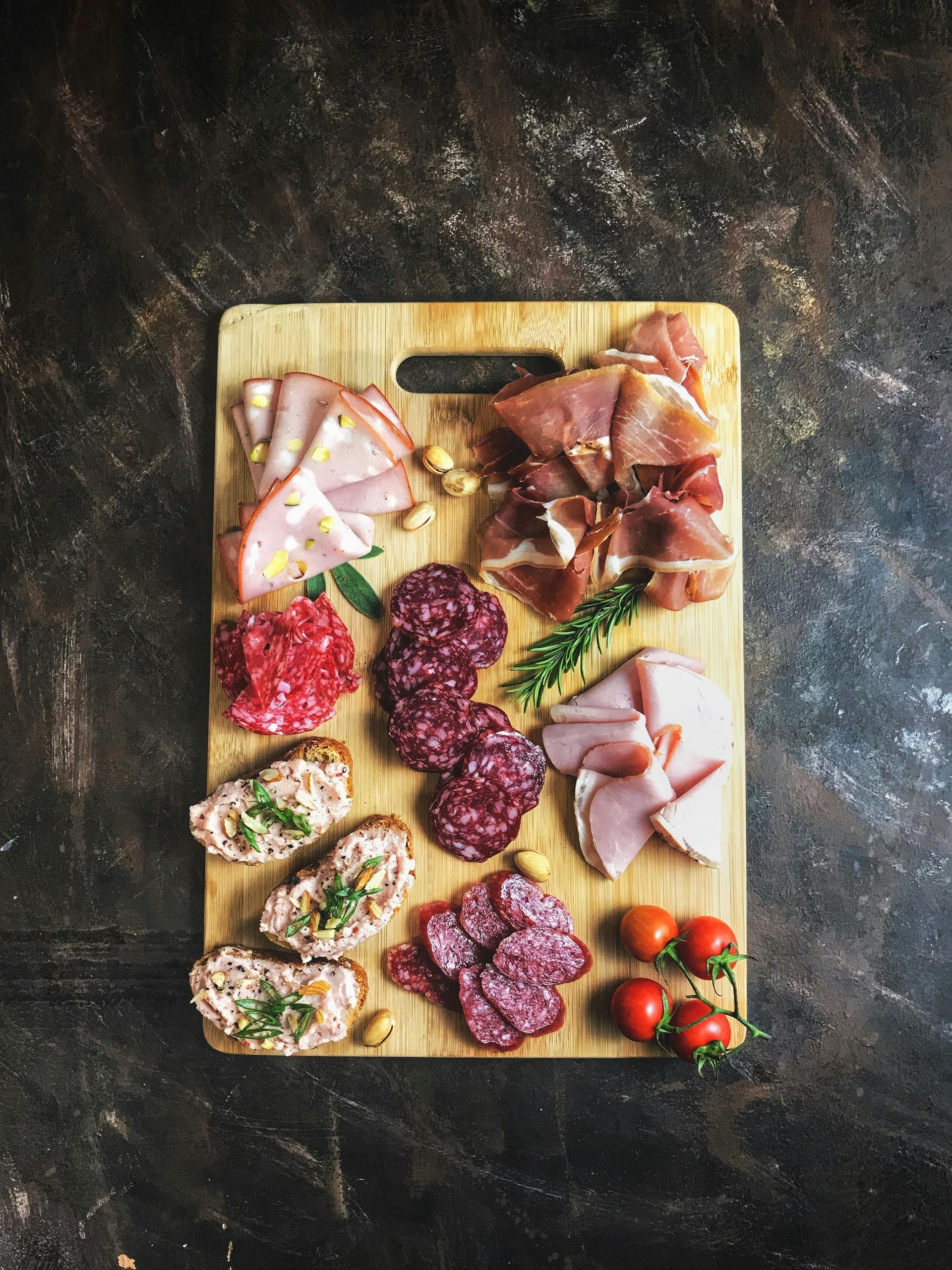Charcuterie board with cured meats, cheese, olives, cherry tomatoes, and herb garnish on a wooden board.