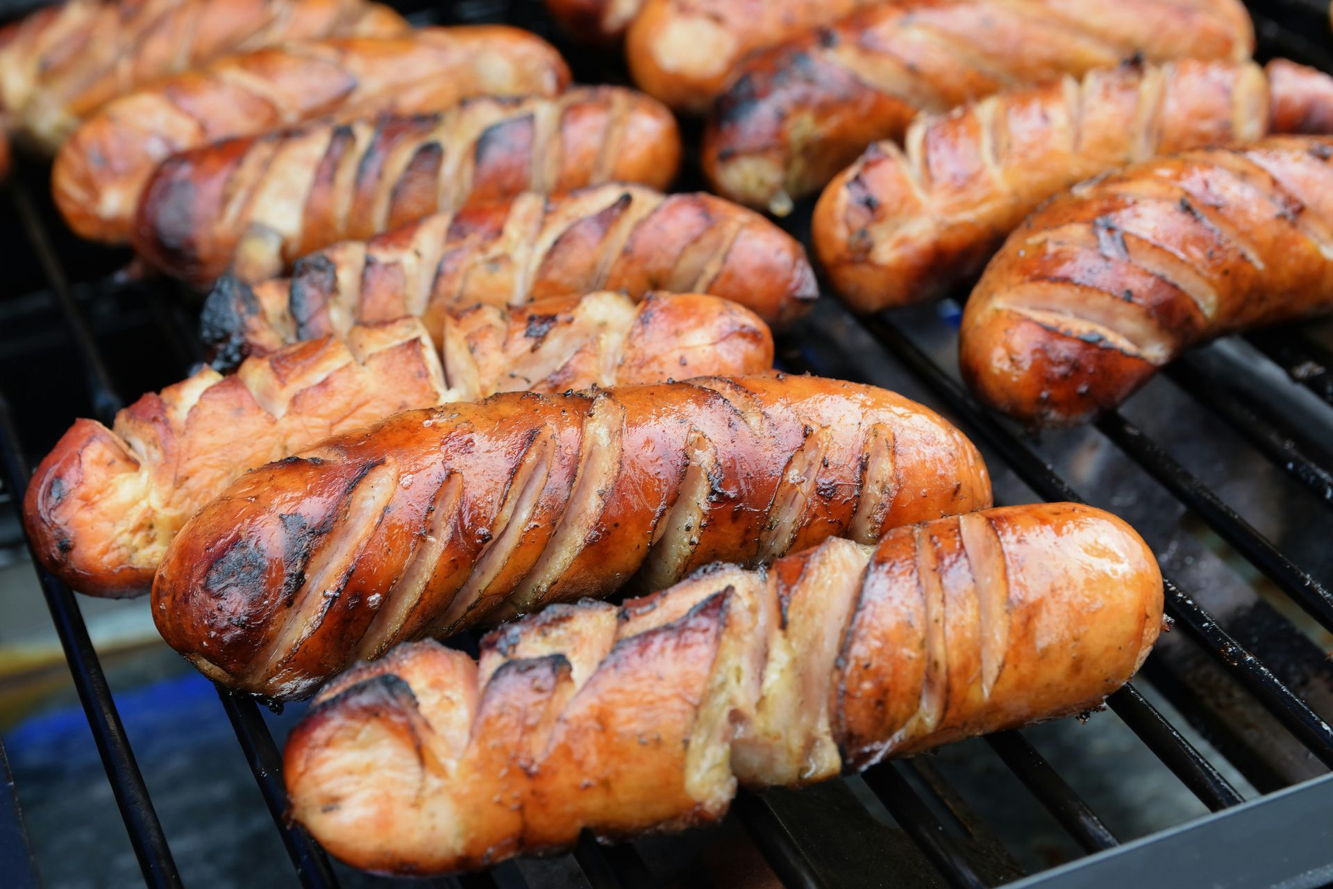 Grilled sausages sizzling on a barbecue grill, with charred stripes and smoky glaze