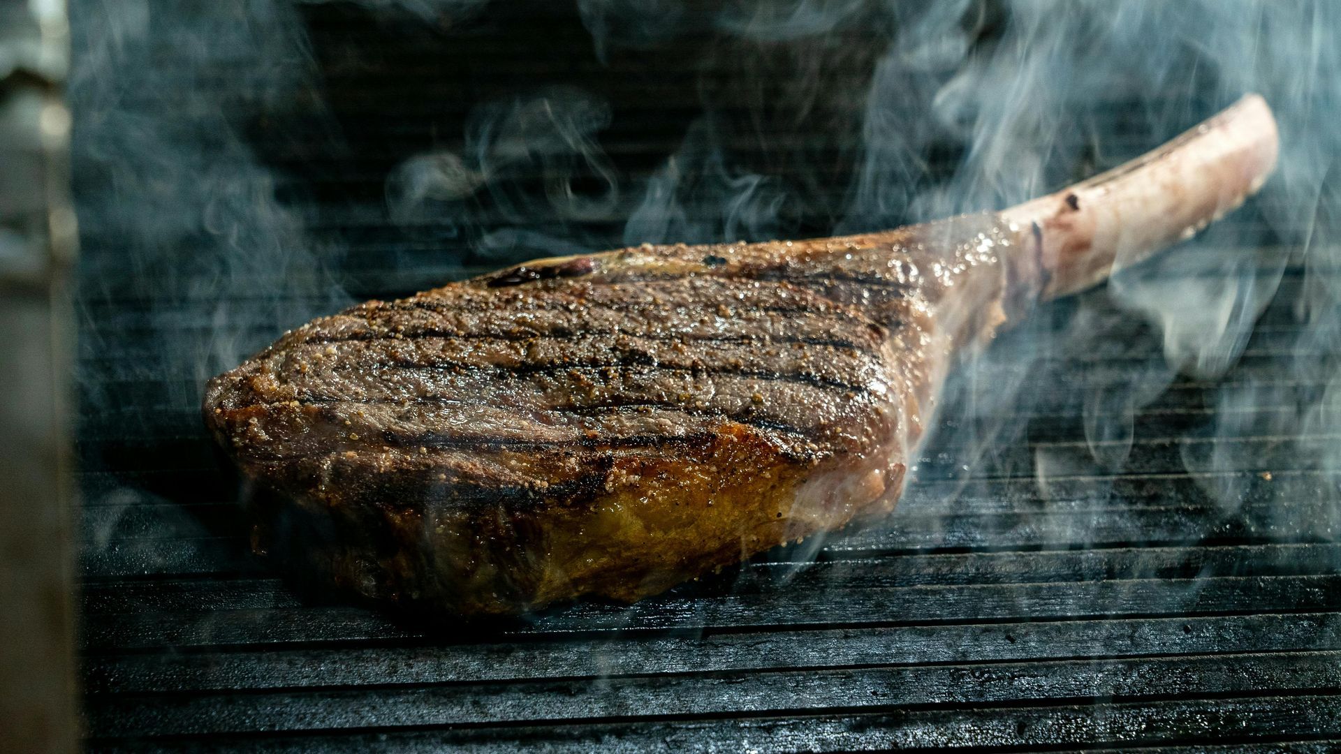 Grilled steak with a bone, sizzling on a smoky barbecue grill