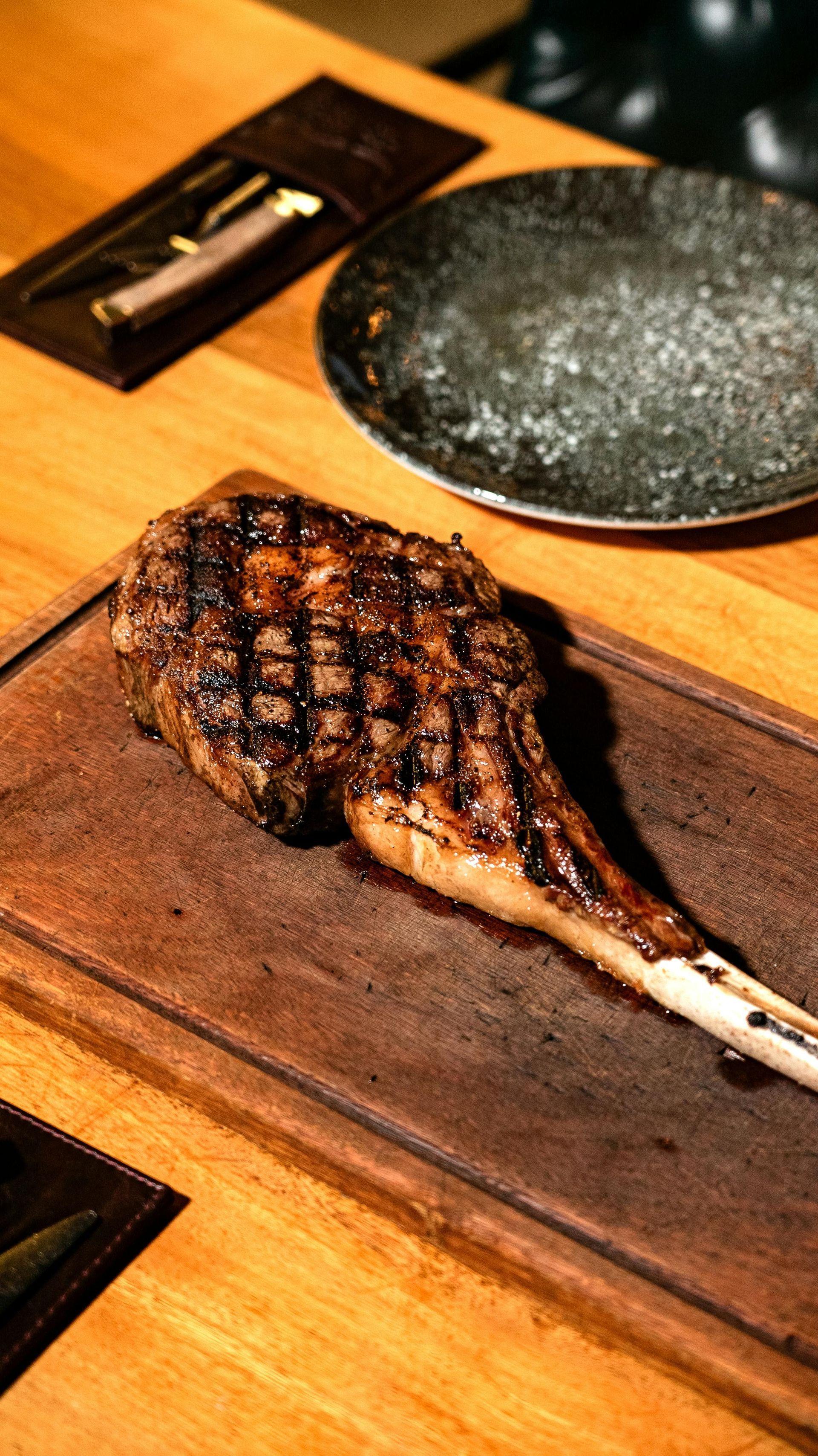 Grilled steak on a wooden board with a hot stone plate and knife on a restaurant table