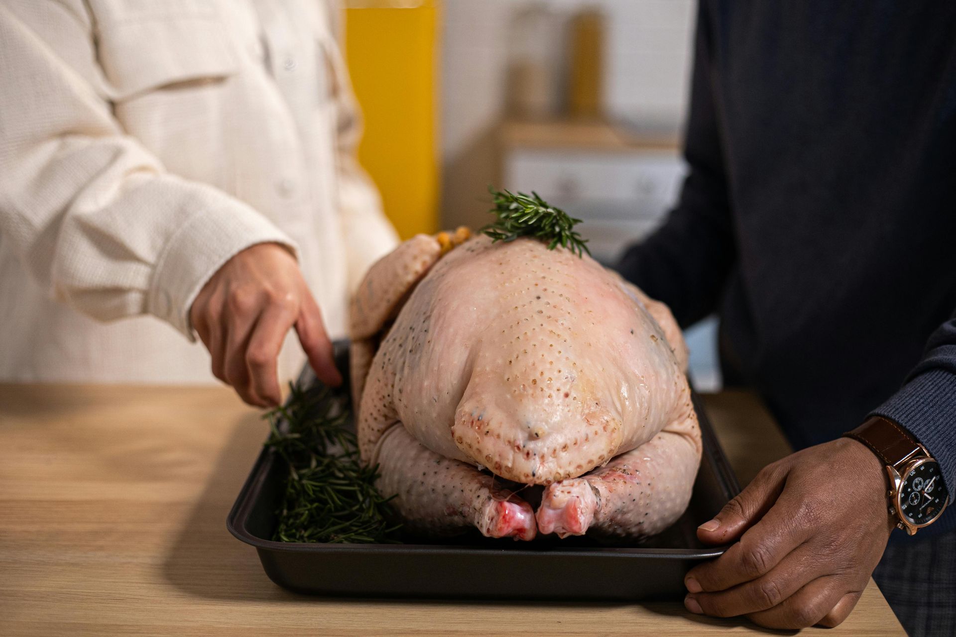 Raw turkey on a roasting pan being held by two people in a kitchen
